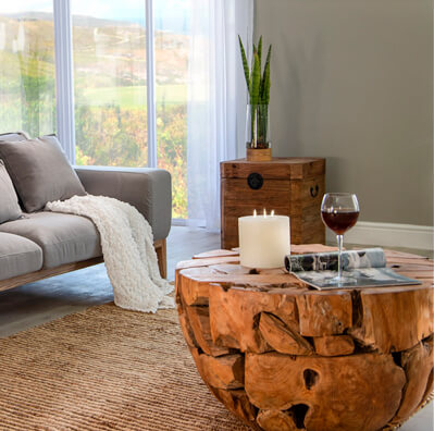 Relaxed living room with round shaped wooden coffee table with a white burning candle, magazine and a glass of red wine on top